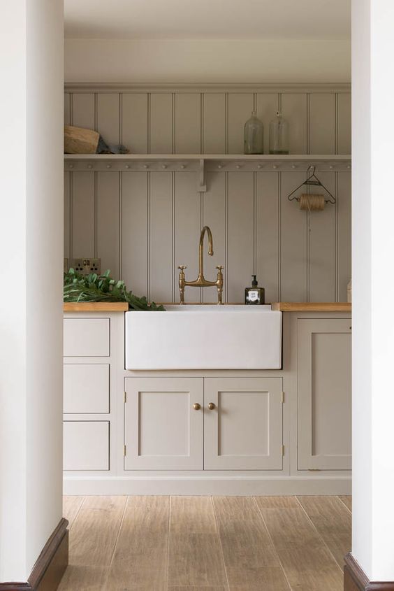 a rustic greige kitchen with shaker cabinets, a matching planked wood backsplash, butcherblock countertops and touches of brass