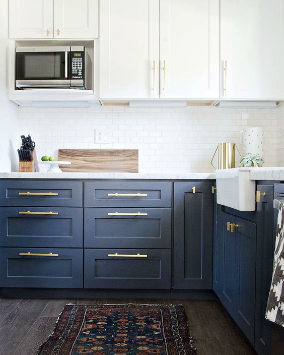 a trendy two tone navy and white kitchen with white countertops and gold hardware that give it a more modern feel