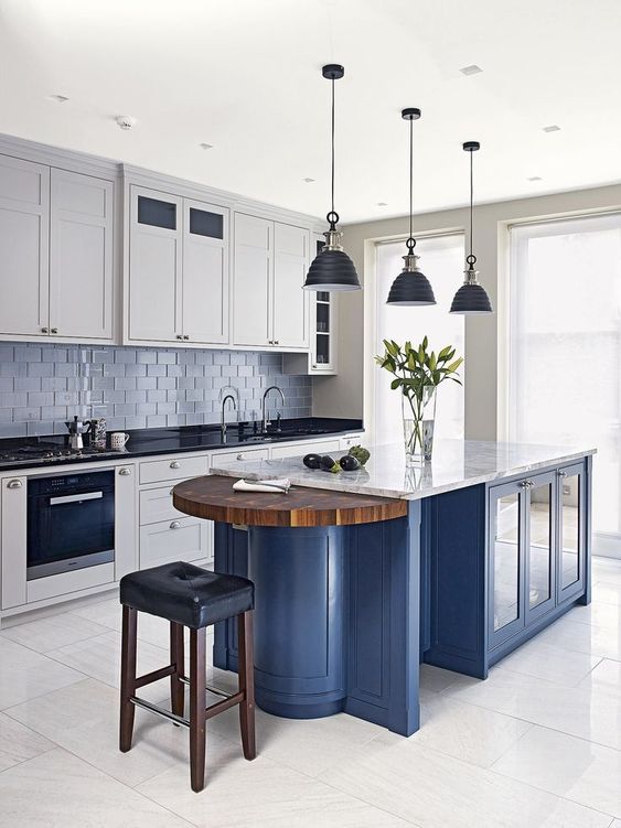 white cabinets with black countertops, a blue kitchen island with a white countertop and a wooden part seem very contrasting